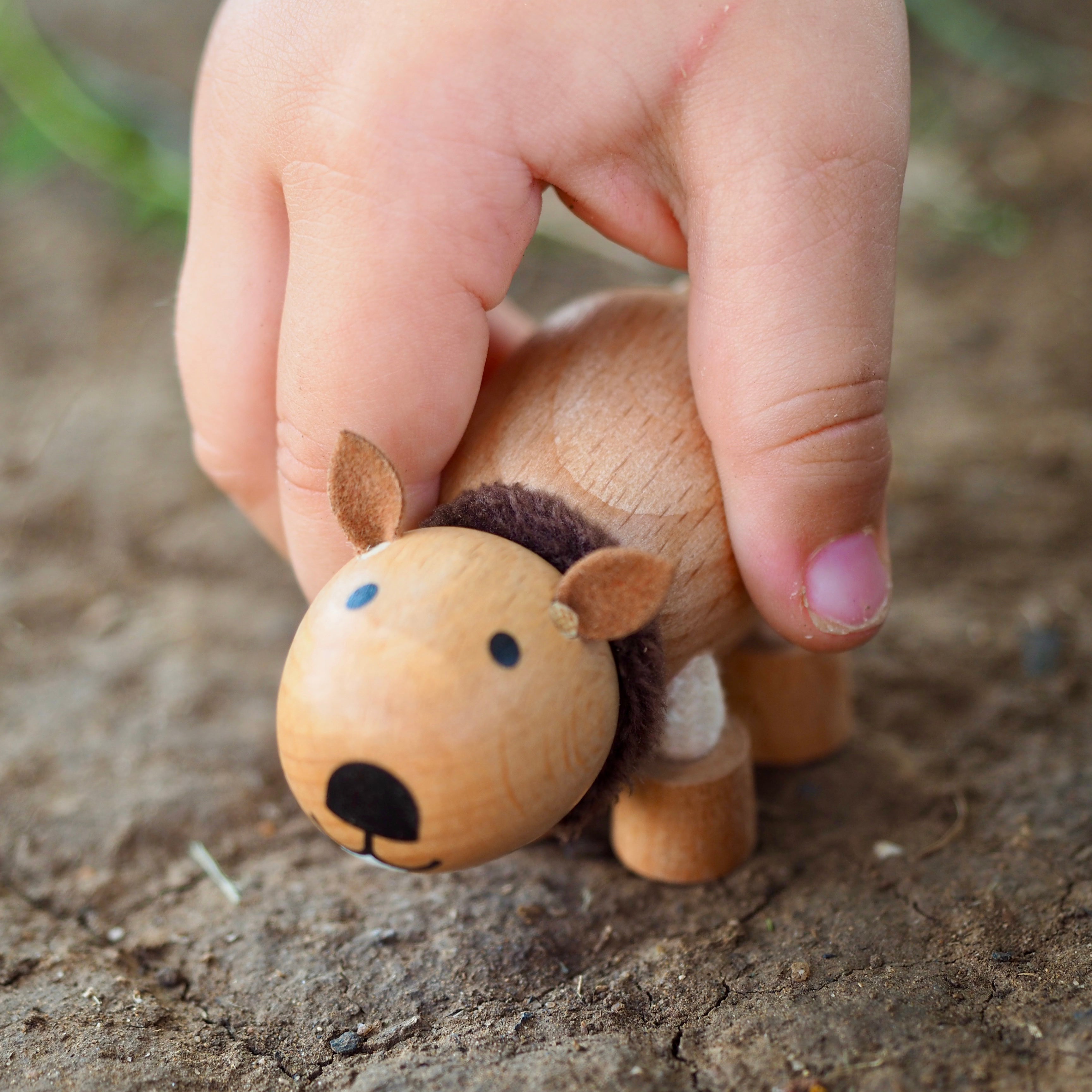 Small wooden wombat figurine held by a child's hand on dirt background