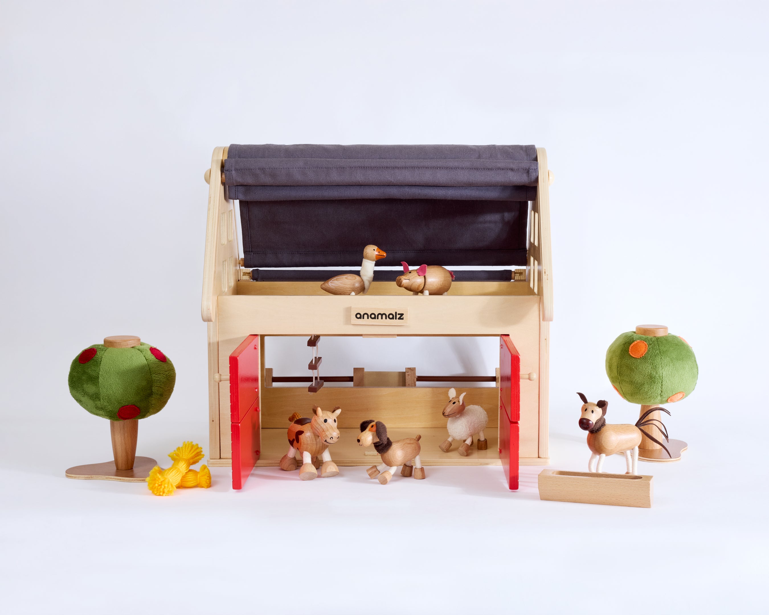 Wooden toy Barnhouse on white background with wooden animal toys around and inside the barn house and two felt wooden toy trees
