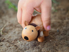 Small wooden wombat figurine held by a child's hand on dirt background