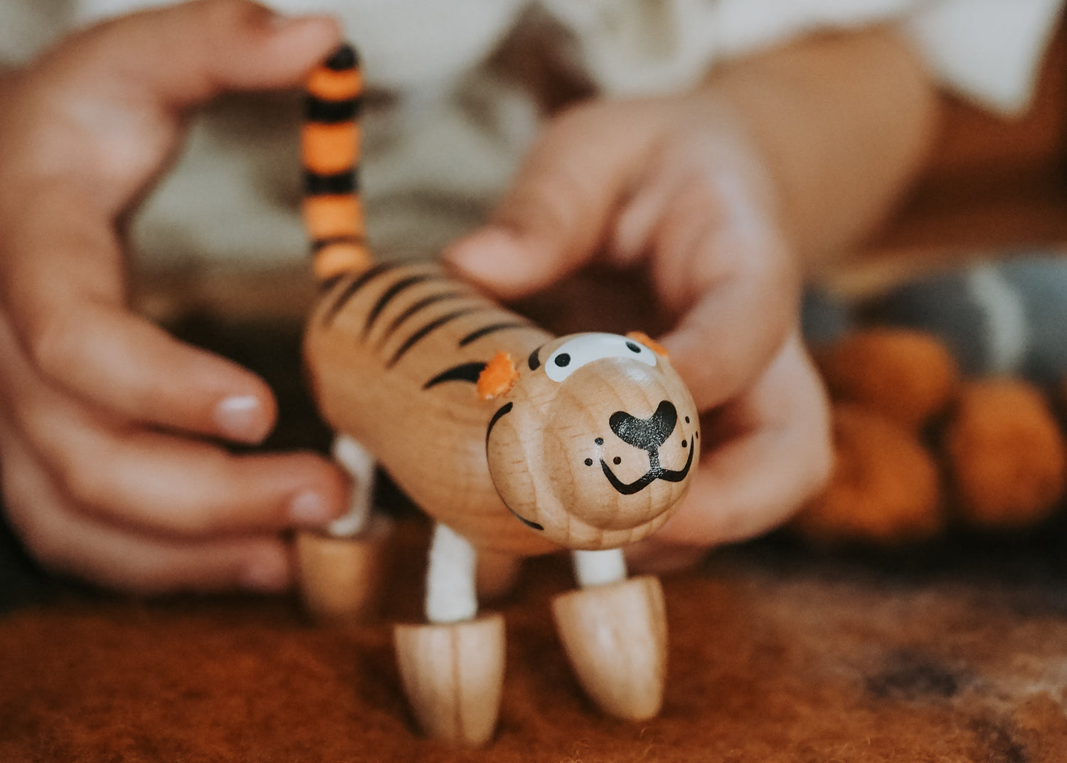 A close-up of a person holding a small wooden tiger toy with orange and black stripes, photographed in a warm indoor setting.