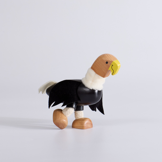 Wooden toy figure of a bird with black wings and a yellow beak on a light gray background