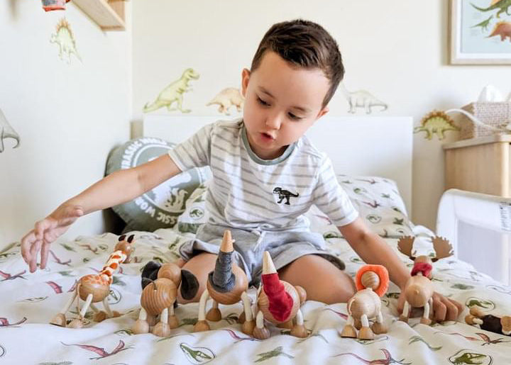 Child playing with toy dinosaurs on a bed in a room with dinosaur-themed decor.