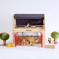 Wooden toy Barnhouse on white background with wooden animal toys around and inside the barn house and two felt wooden toy trees