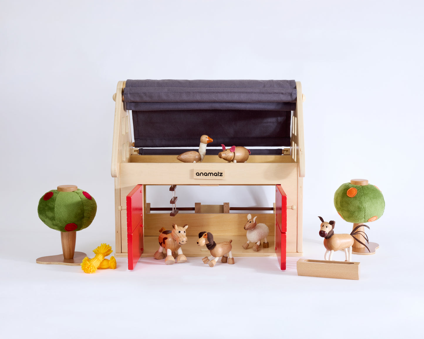 Wooden toy Barnhouse on white background with wooden animal toys around and inside the barn house and two felt wooden toy trees