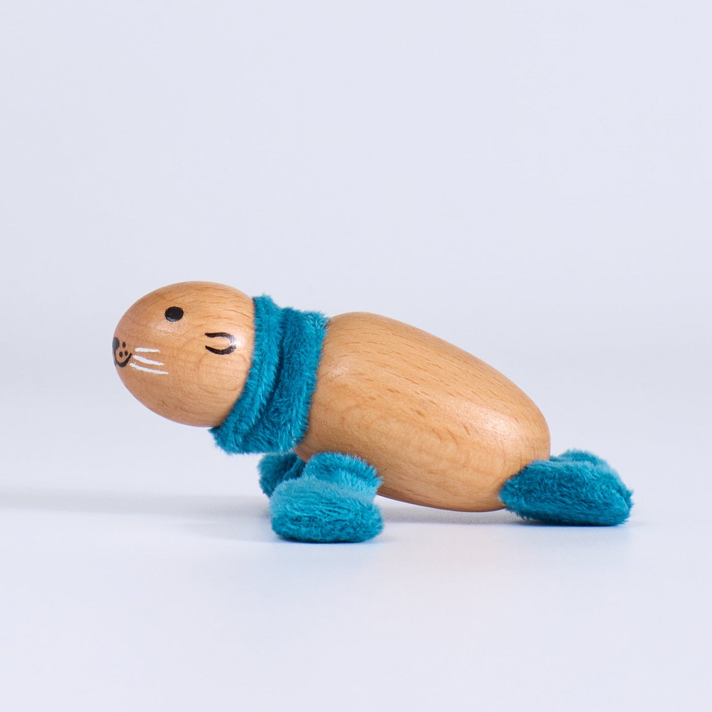 Wooden toy seal with a blue scarf on a light gray background