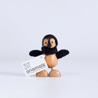 Wooden penguin figurine with black wings and a white card displaying 'anamaiz' on a light gray background