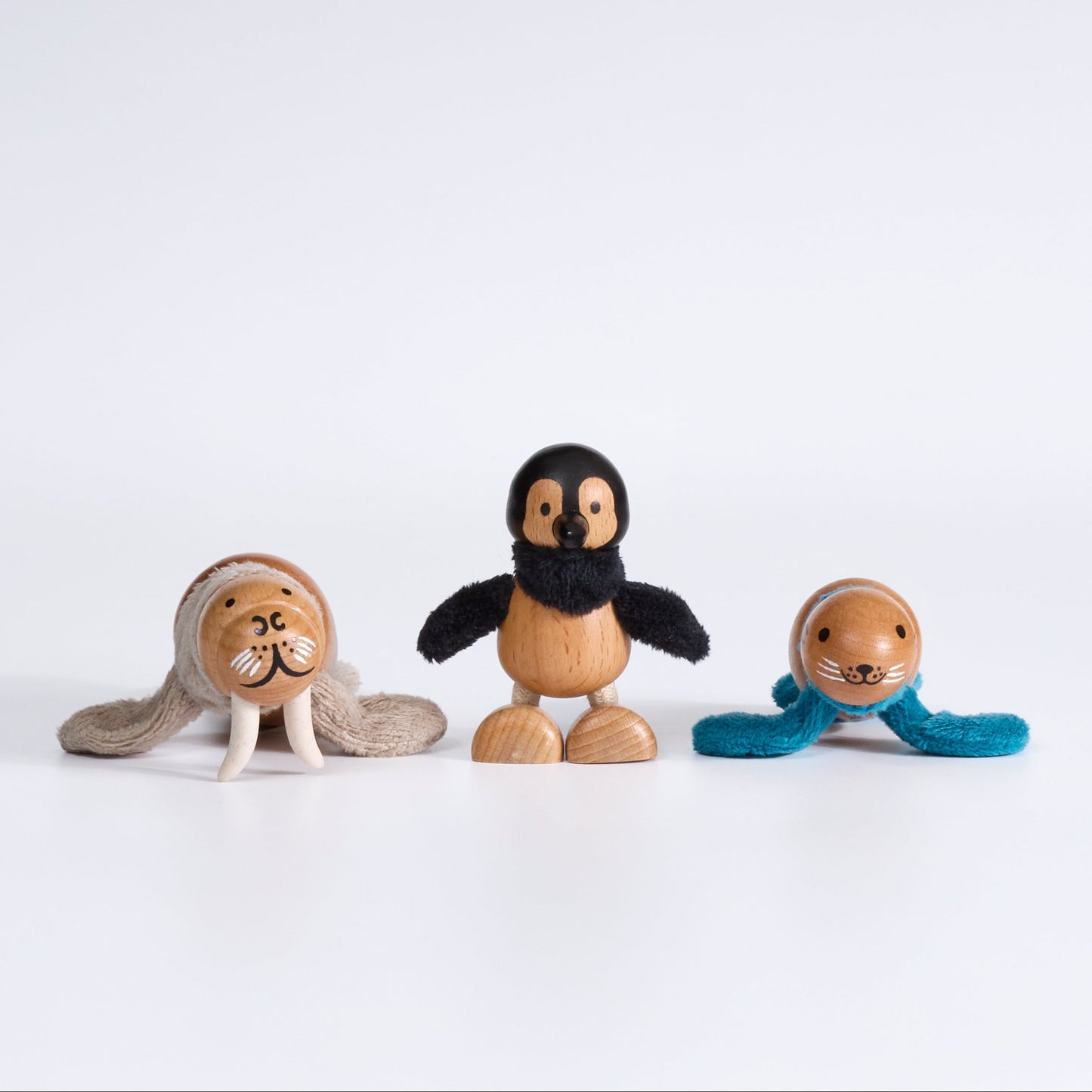 Three wooden walrus, penguin and seal figurines on a white background